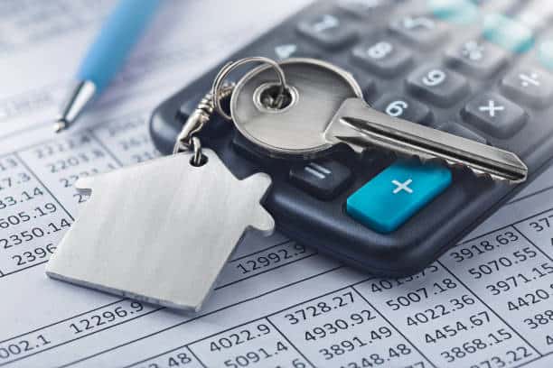 House-shaped keychain and keys on a calculator, placed on financial documents with numerical data.