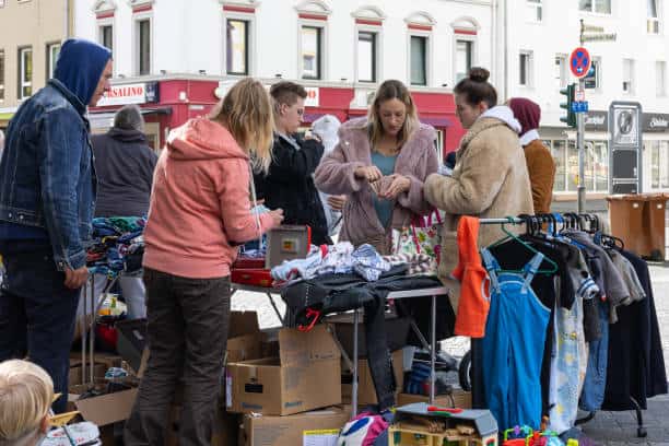 People browsing clothes and items at an outdoor flea market, with boxes and racks of clothing on display.