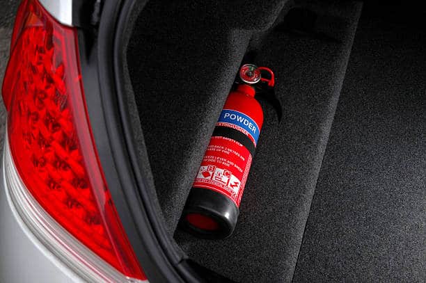 A red powder fire extinguisher lies in the trunk of a car.