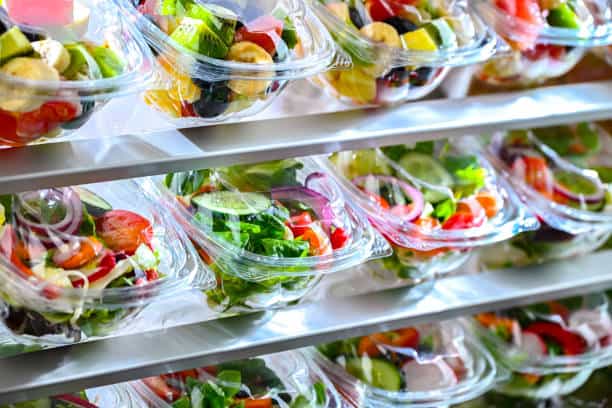 Shelves filled with rows of pre-packaged salads in clear plastic containers.