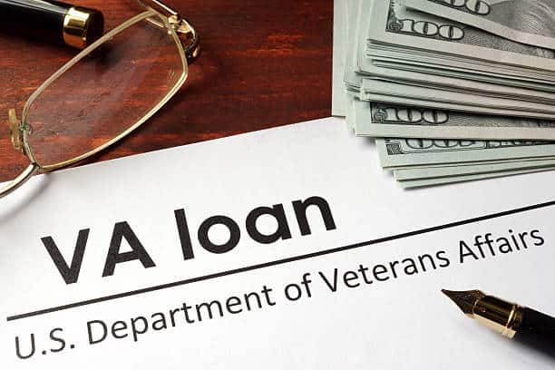 VA loan document with a pen, glasses, and a stack of hundred-dollar bills on a wooden table.