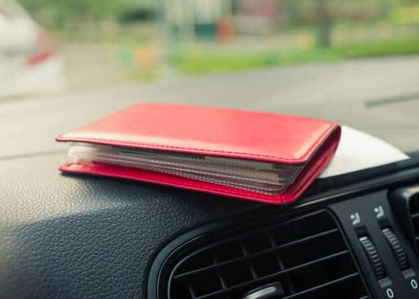 Red wallet placed on a car dashboard near the air vent.