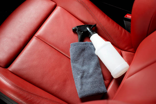 A spray bottle and dark cloth are placed on a red leather car seat.