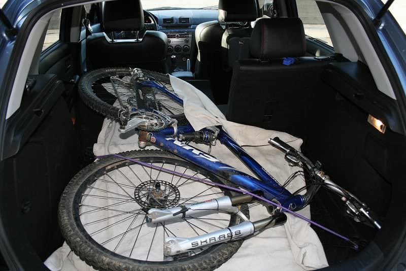 A bicycle is placed inside the trunk of a car, resting on a white blanket.