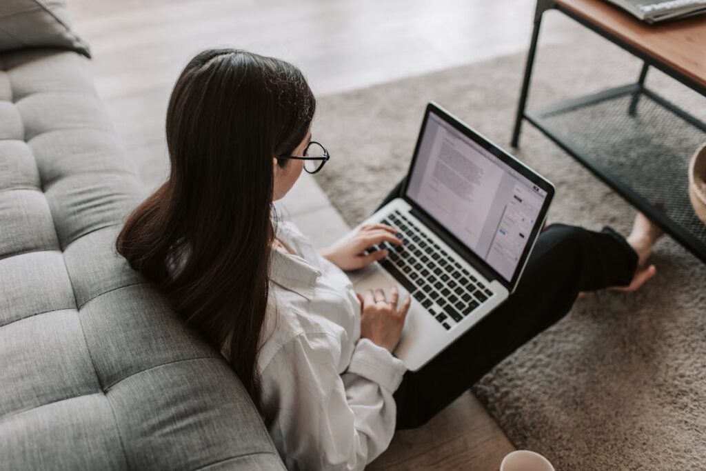 Person sitting on the floor next to a sofa, working on a laptop.