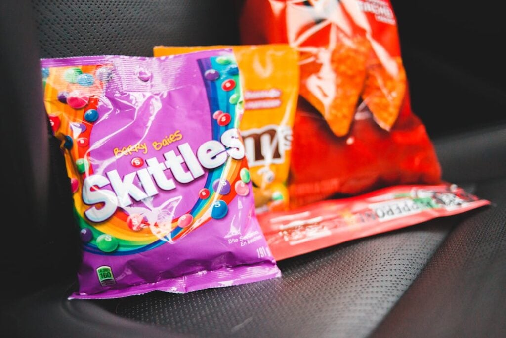 Bags of Skittles, Doritos, and M&M's on a car seat.