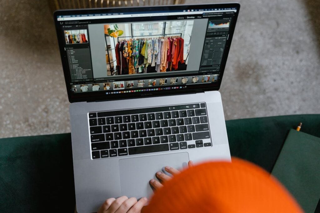 Person using a laptop to edit a photo of a clothing rack with colorful garments.