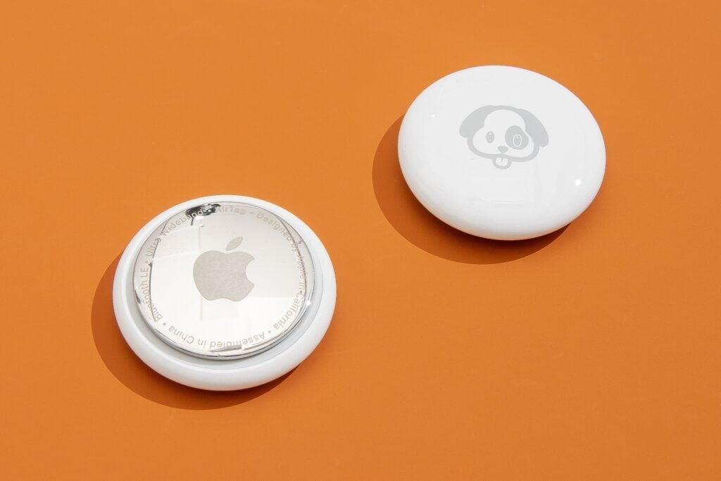 Two white circular devices on an orange surface; the left one shows a metallic Apple logo, and the right one has a cartoon dog face.