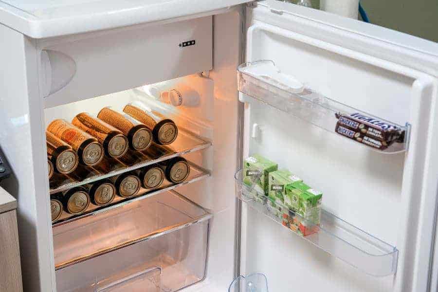 Open fridge with soda cans inside and juice boxes and a chocolate bar in the door compartments.