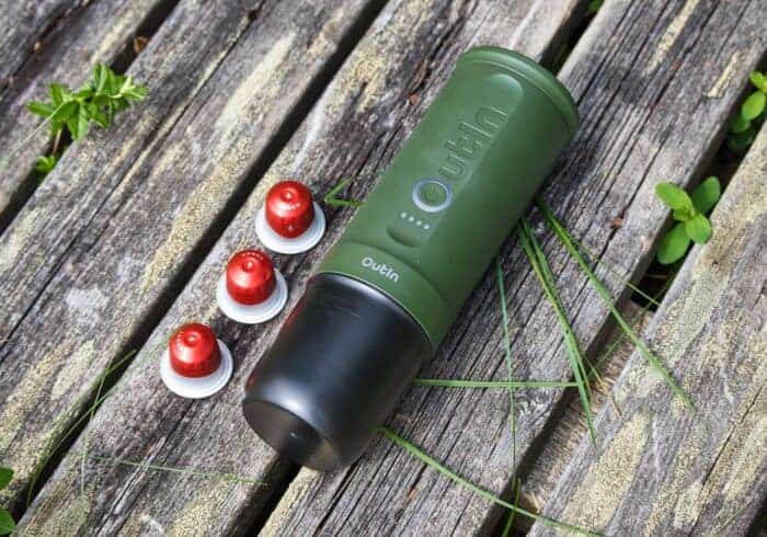 Green portable coffee maker on a wooden surface next to three red coffee pods.