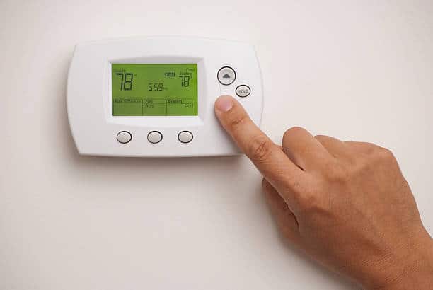 Hand adjusting settings on a digital thermostat mounted on a wall.