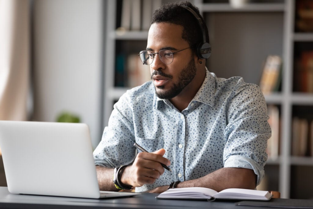 A man wearing headphones is diligently working on a laptop to earn a good salary.