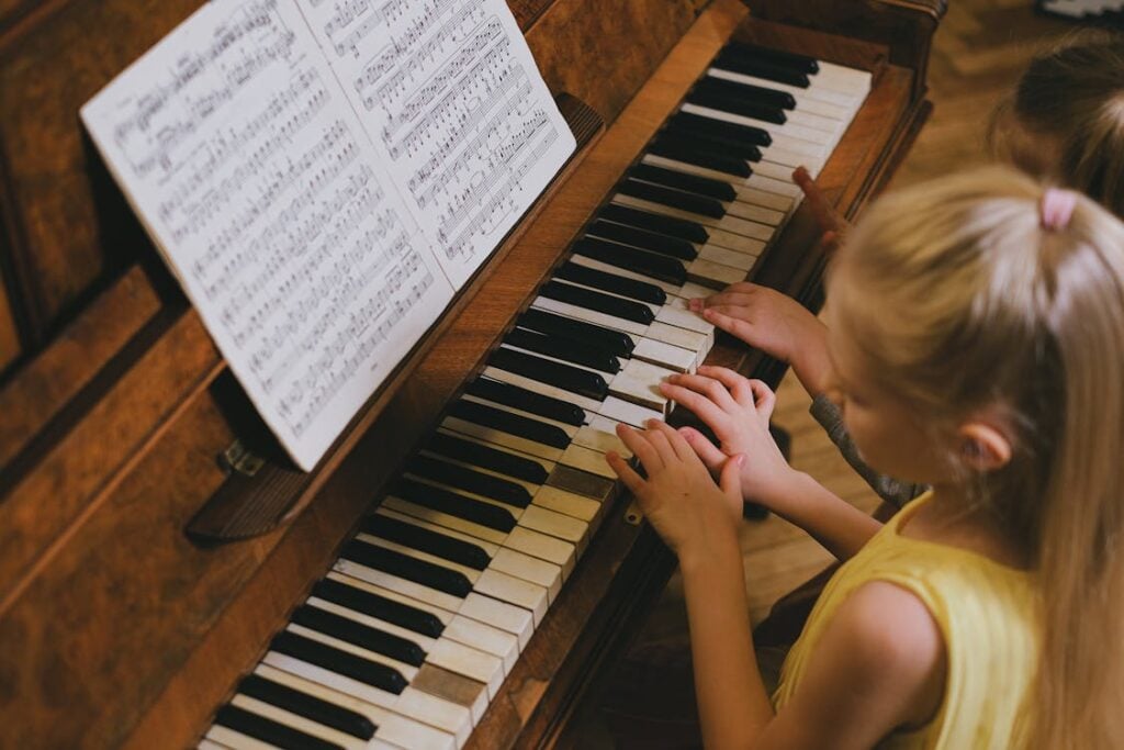 Two children playing a piano together, with sheet music on the stand in front of them.