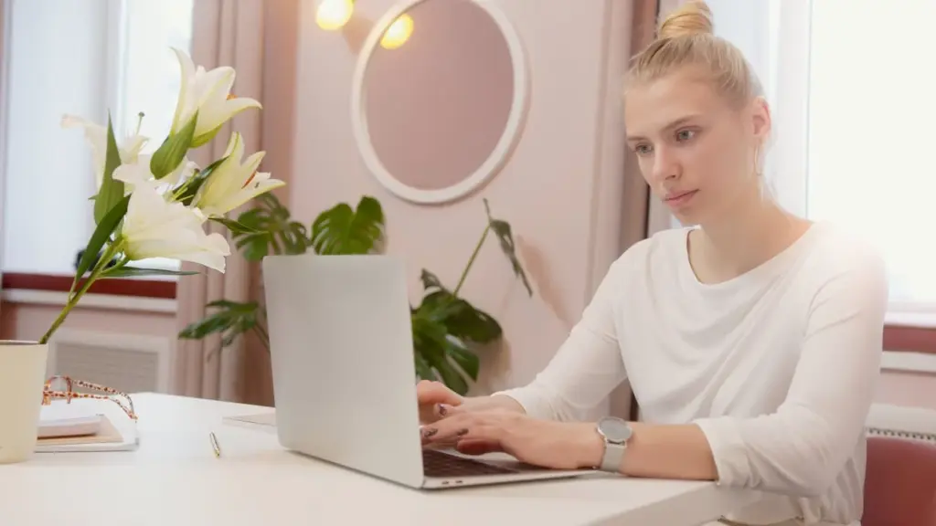 Person typing on a laptop at a desk with white lilies, a notebook, and a wall mirror in the background.