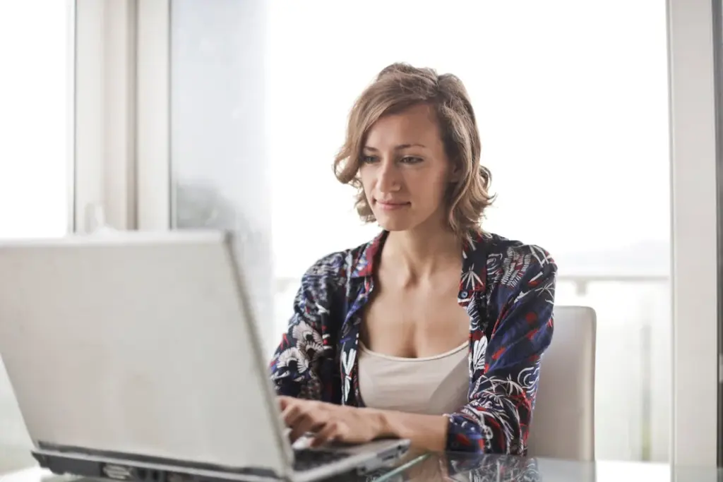 Woman sitting at a desk using a laptop in a bright room.