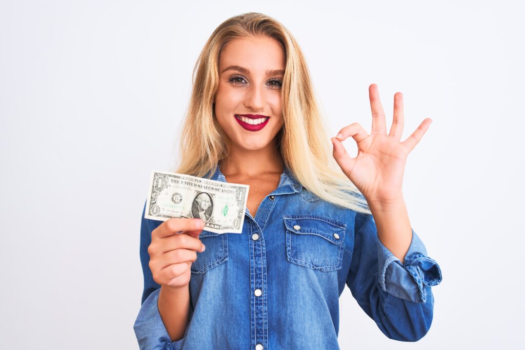 Person in a denim shirt holding a one-dollar bill and making an 