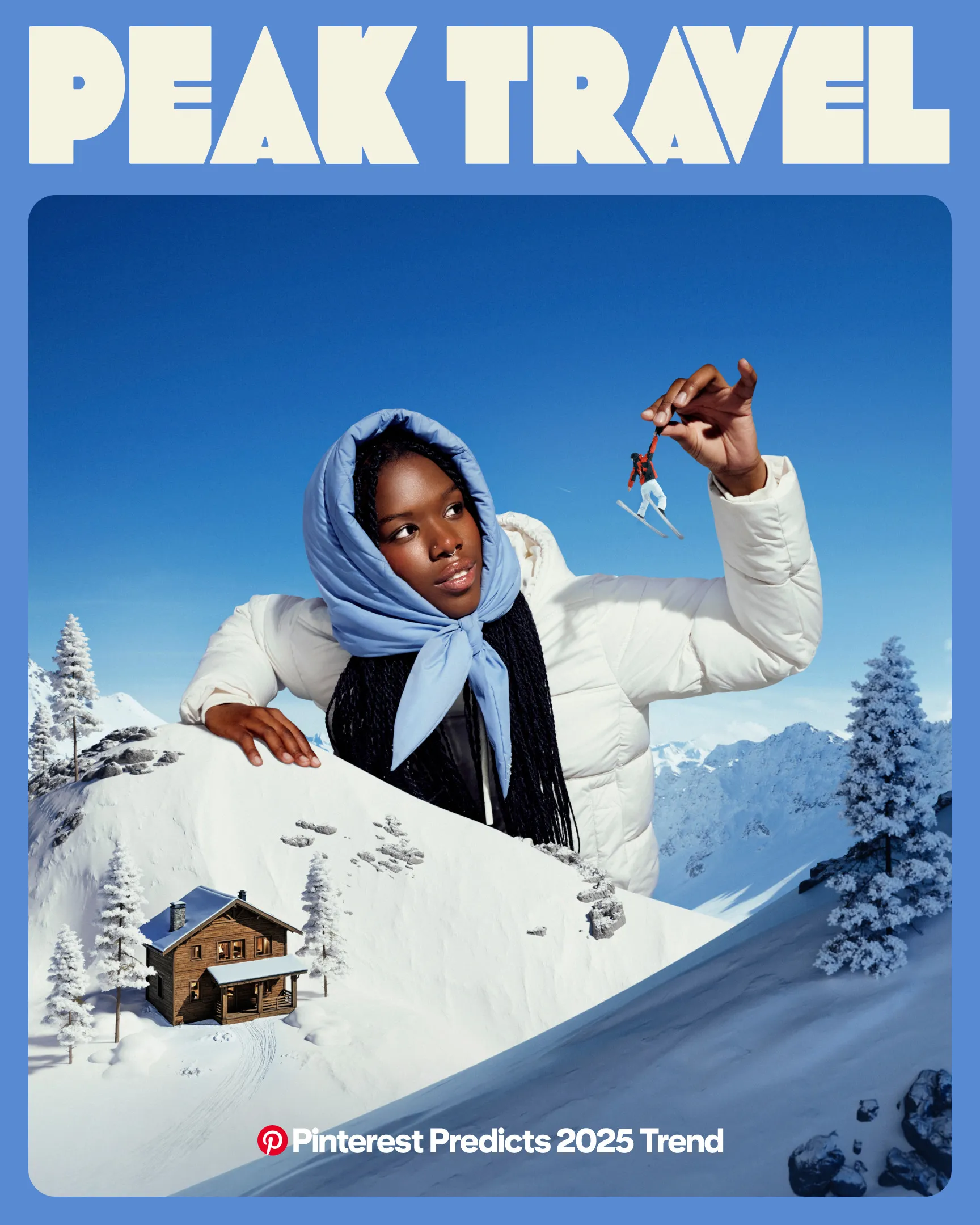 A woman stands against snowy rocks in a white puffy coat and periwinkle scarf. She is examining a tiny toy skier that she has picked up from a miniature scene of a ski resort.