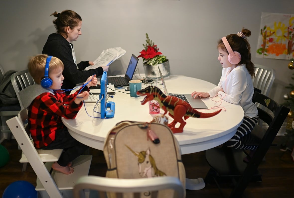 A mom and two kids all sit at a table with laptops