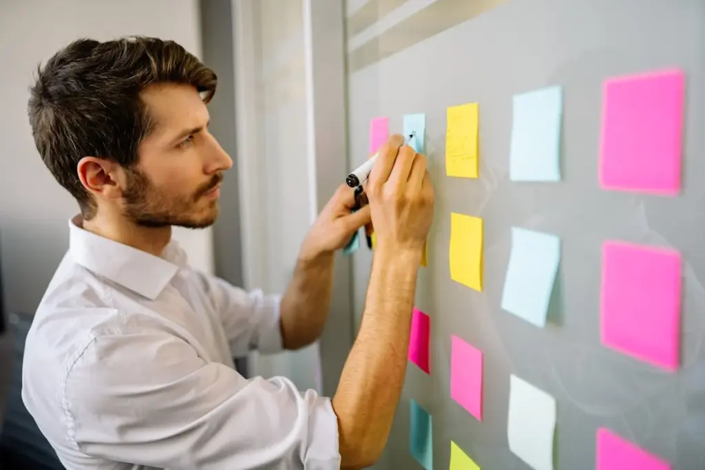 A man writes on colorful sticky notes arranged on a glass wall.